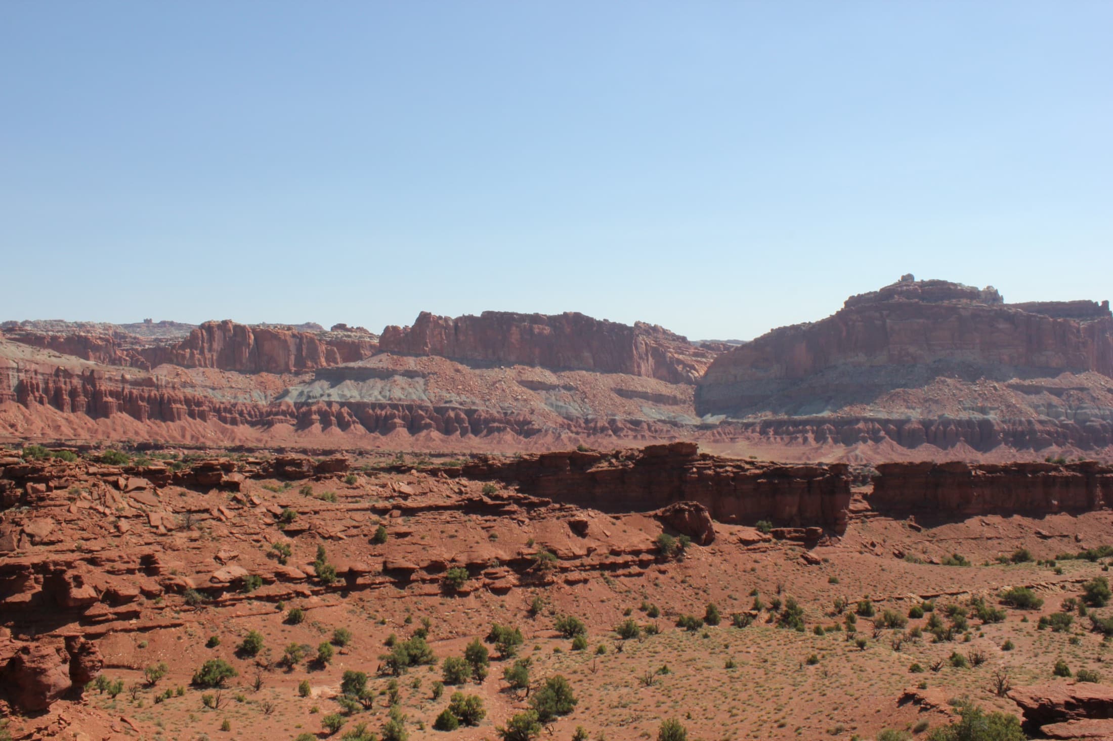 Scenic vista of the rugged red and tan sandstone cliffs and canyon ridgeline of Capitol Reef National Park, Utah, under a clear sky