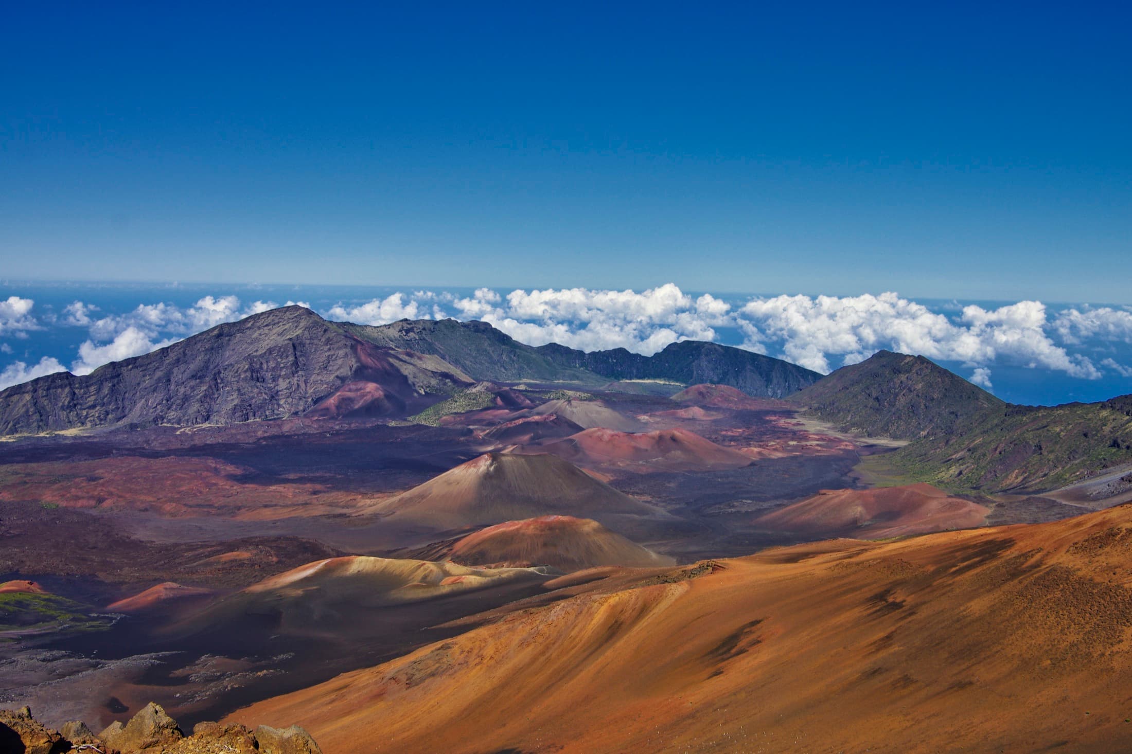 The volcanic crater of Haleakala National Park on Maui, Hawaii, a vast reddish-brown basin of cinder cones and barren lava under a clear sky, viewed from the summit at nearly 3,000 meters elevation