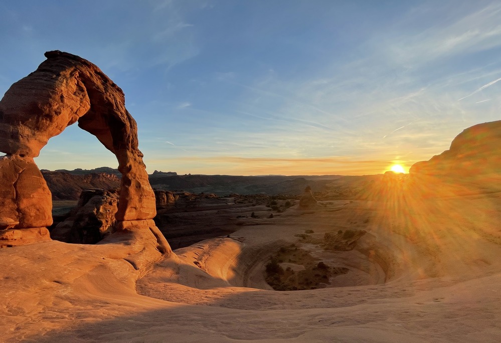 Delicate Arch glowing at sunset with desert cliffs behind it