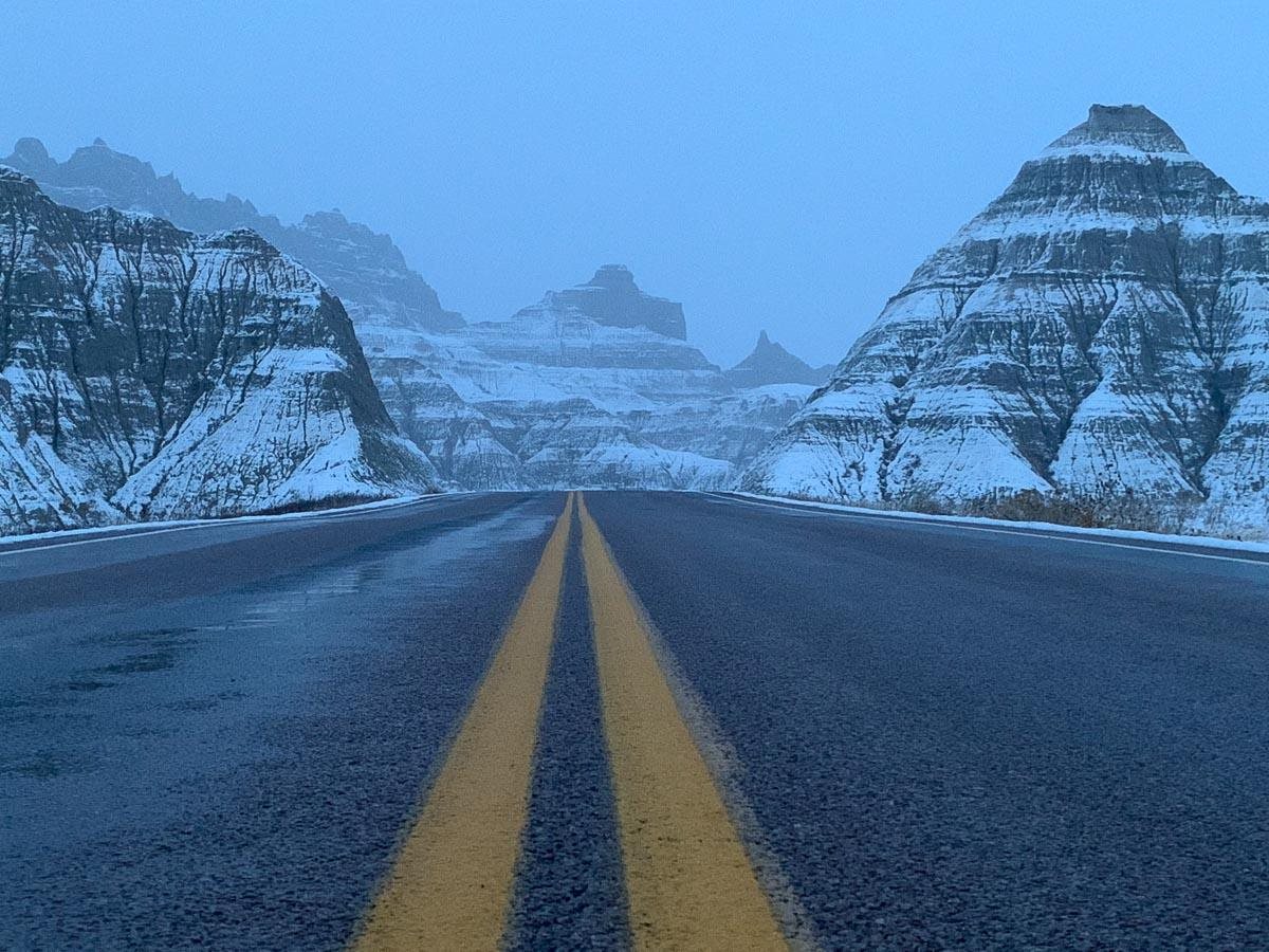 A road running between snow-covered Badlands formations