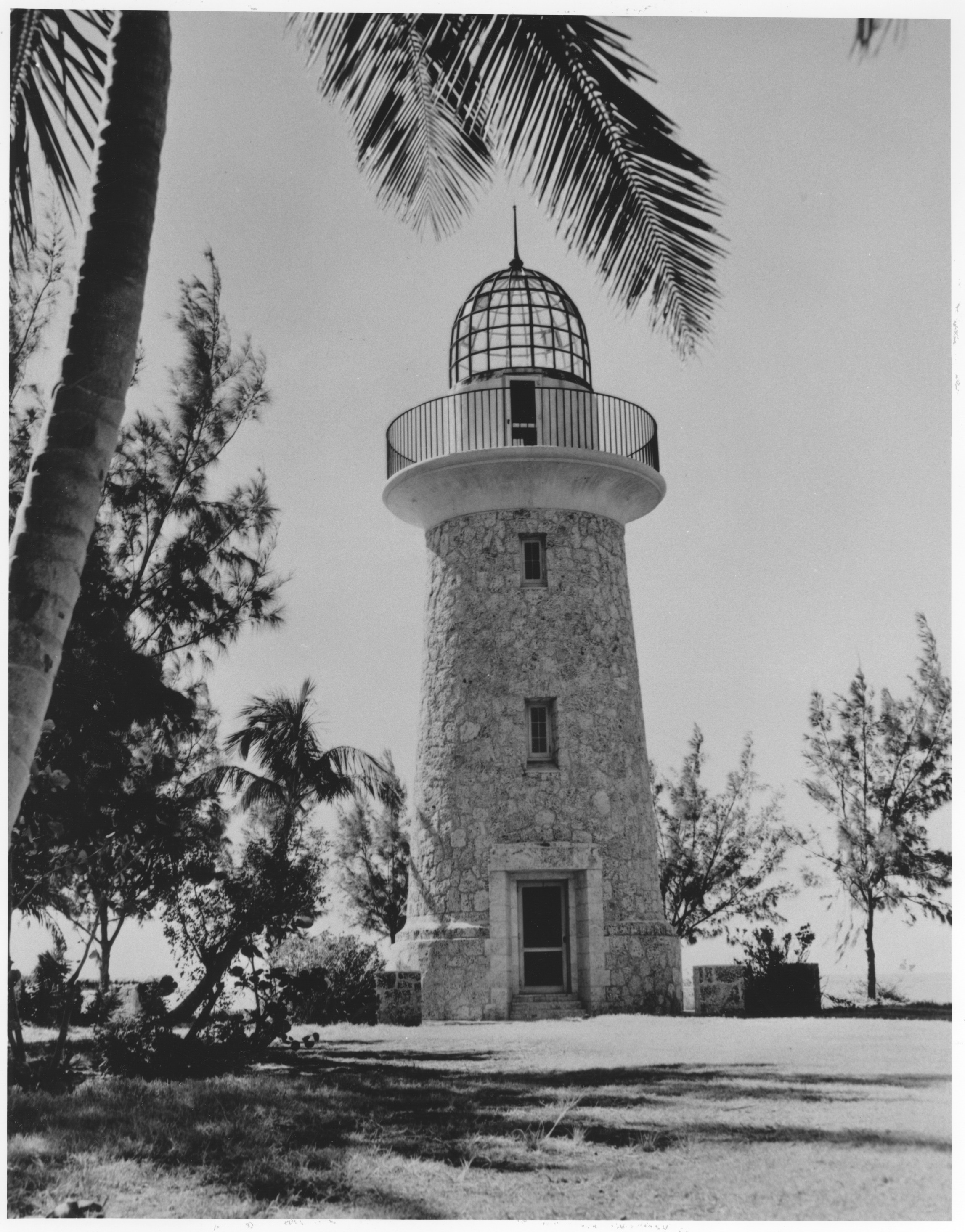 The white Boca Chita lighthouse rising above palms and blue water