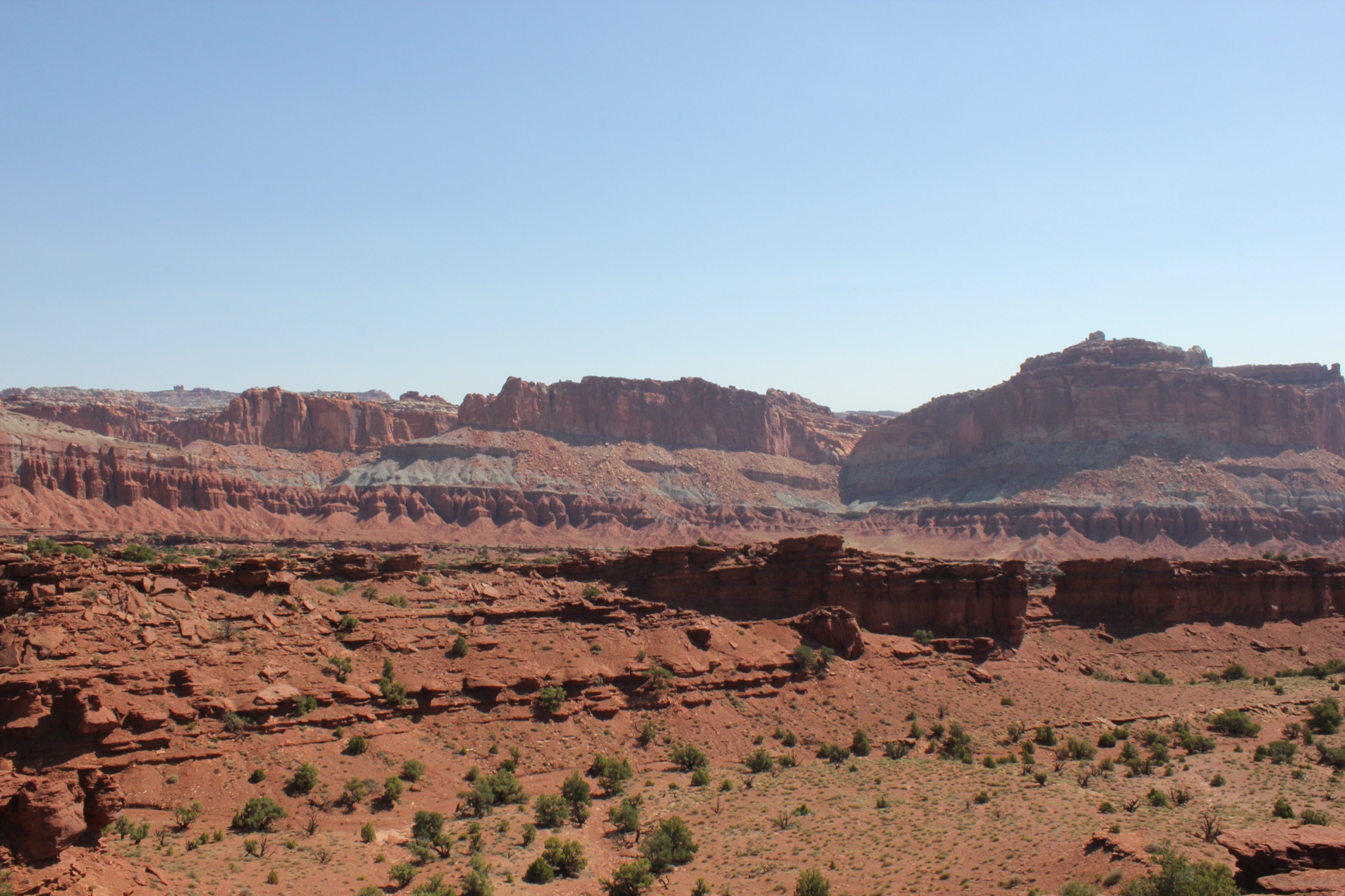 Scenic vista of the rugged red and tan sandstone cliffs and canyon ridgeline of Capitol Reef National Park, Utah, under a clear sky