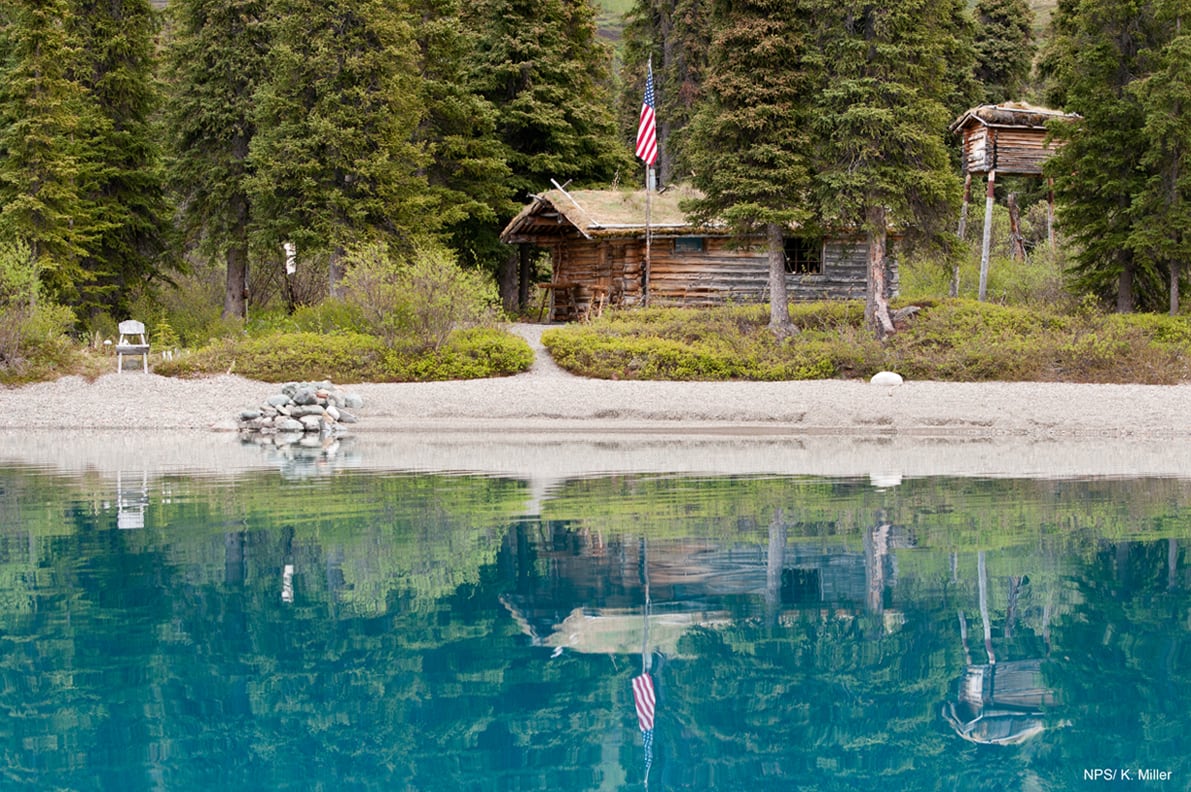 Richard Proenneke's cabin reflected in calm water at Twin Lakes