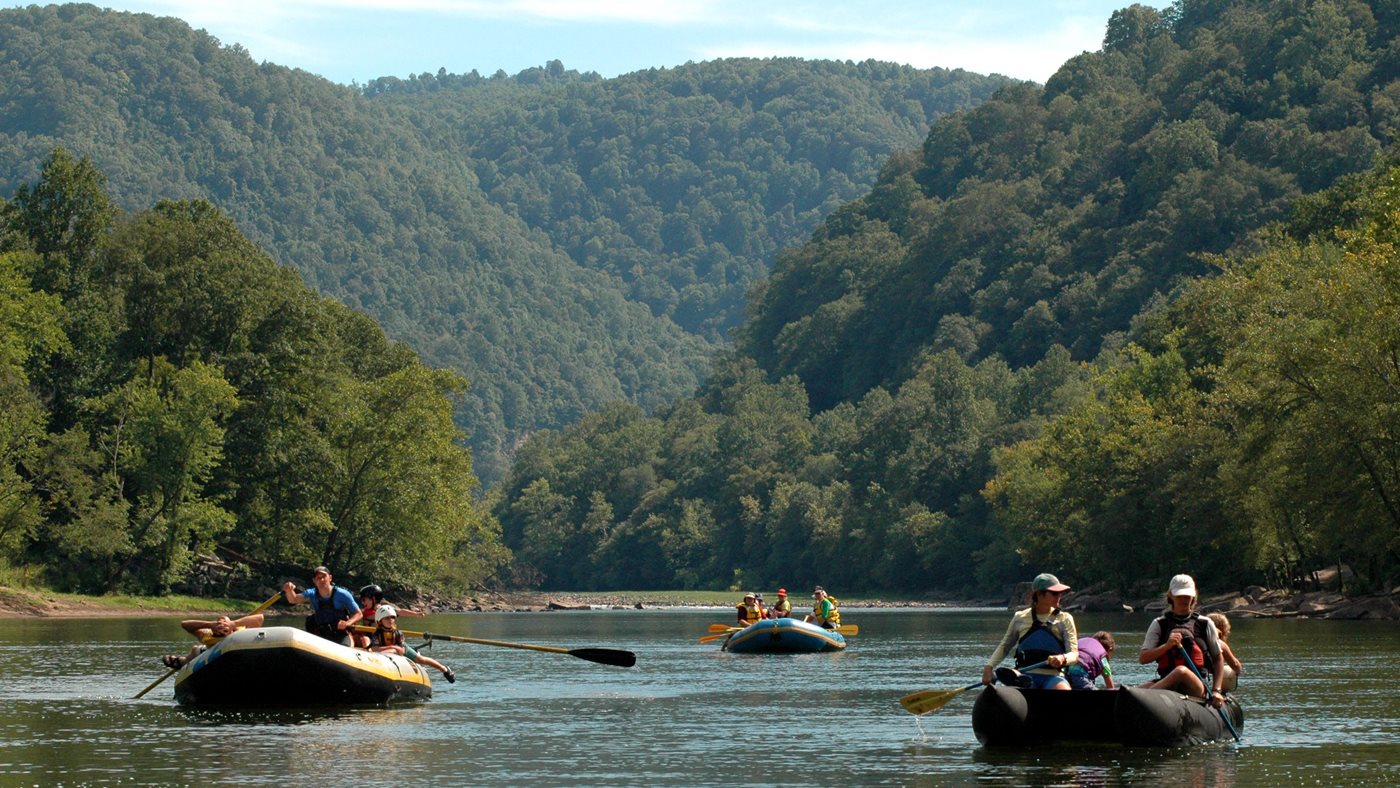 Boaters paddling on the New River below wooded gorge walls