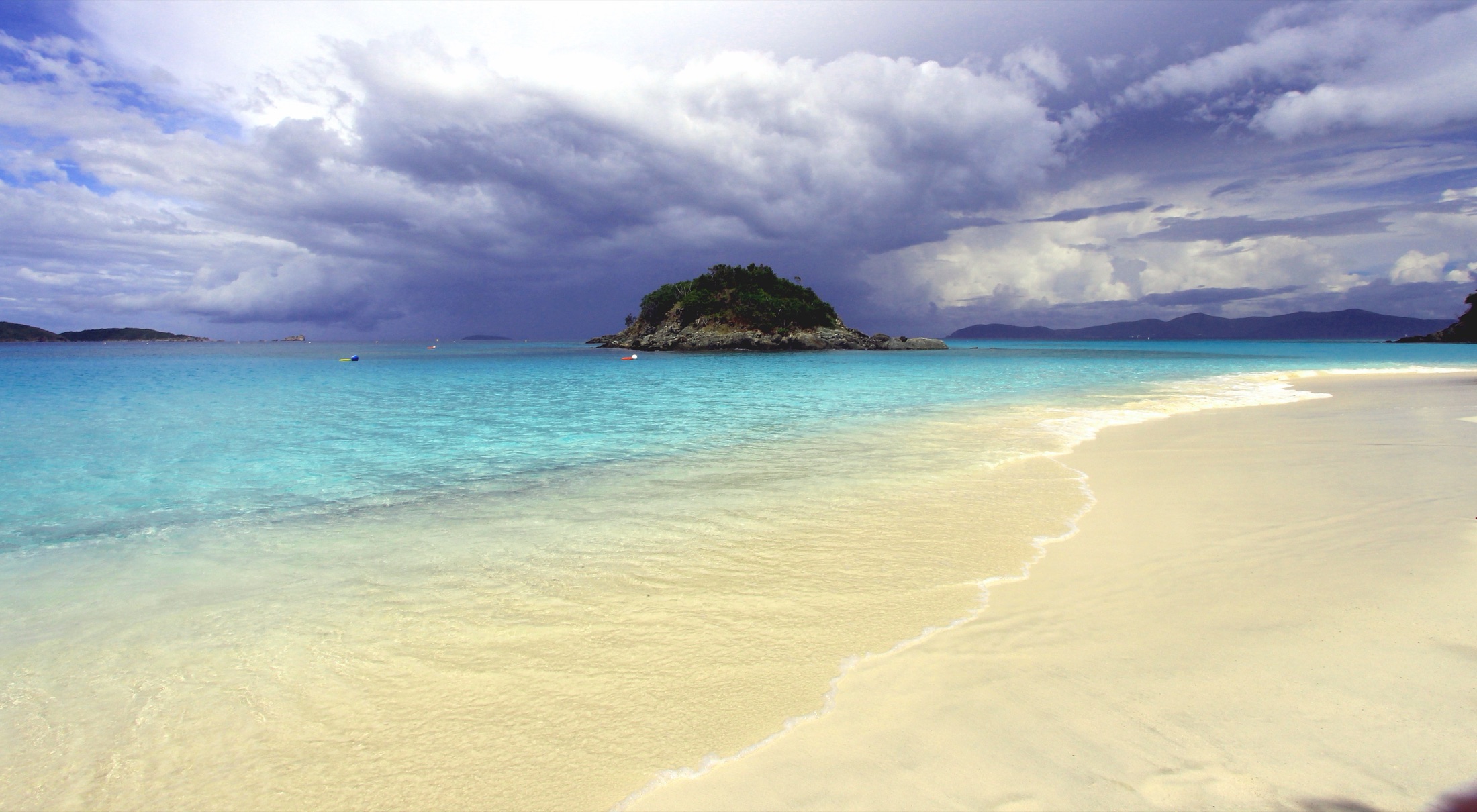 The turquoise waters and white-sand crescent of Trunk Bay seen from above in Virgin Islands National Park on St. John, with lush green hillsides framing the beach and offshore islands on the horizon