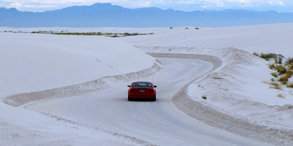 A red car driving Dunes Drive through white gypsum dunes
