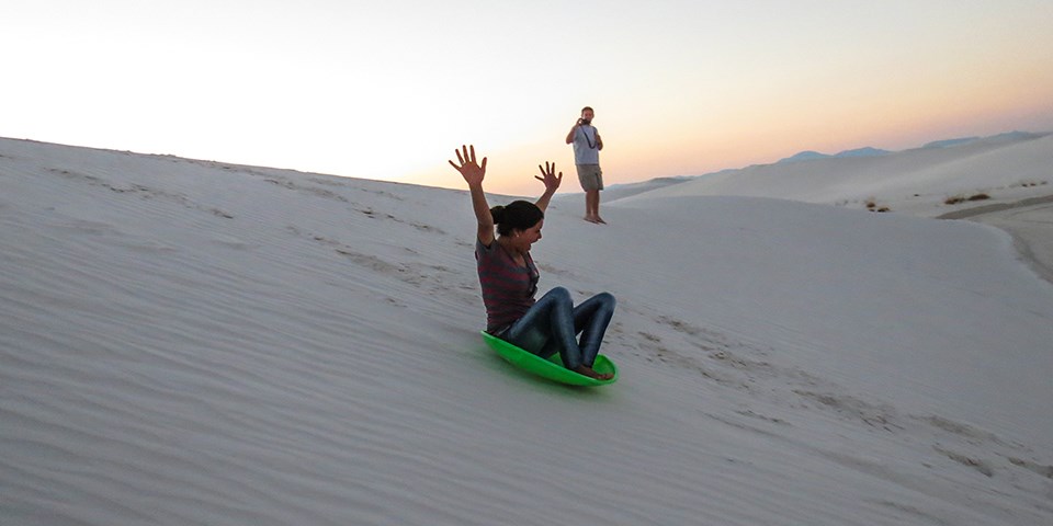 A visitor sledding down a white gypsum dune
