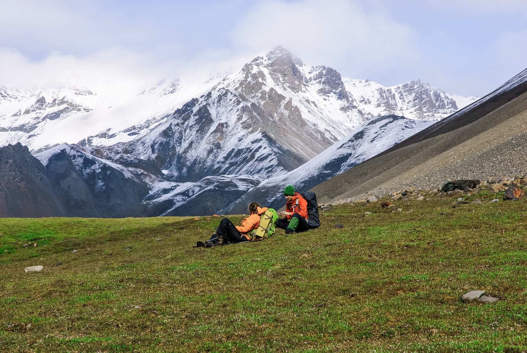 Backpackers sitting in alpine meadow below snowy Mentasta Mountains